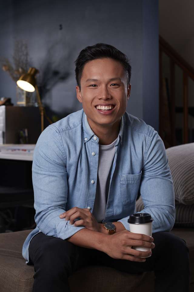 An online student sitting on a couch smiling and holding a takeaway coffee