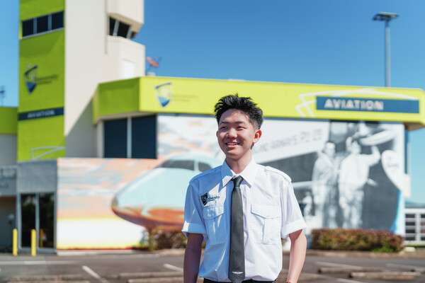 Smiling aviation student in uniform stands outside a university aviation building