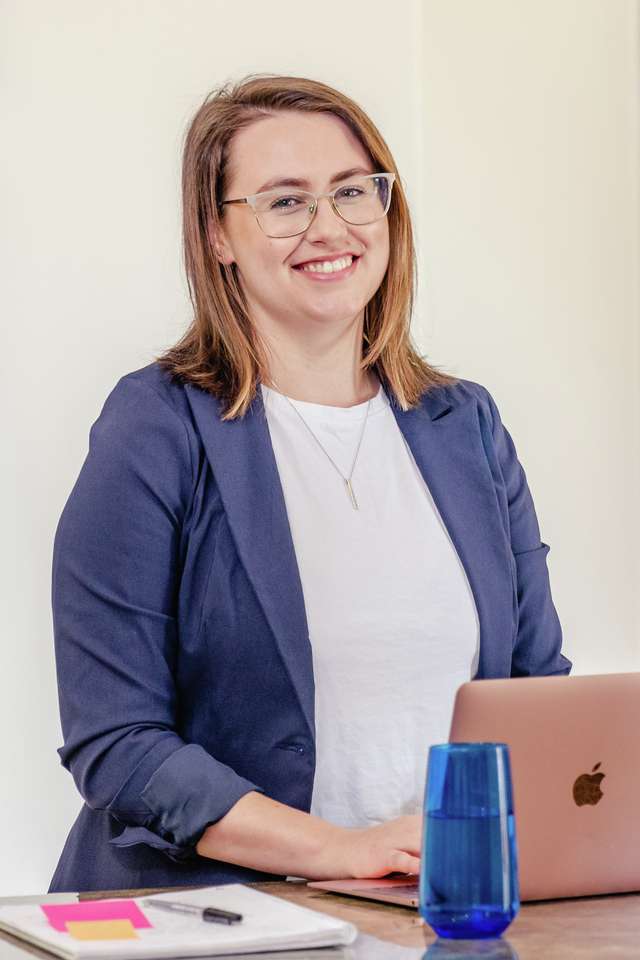 Student smiling and sitting at laptop with notepad with bright painting in background.