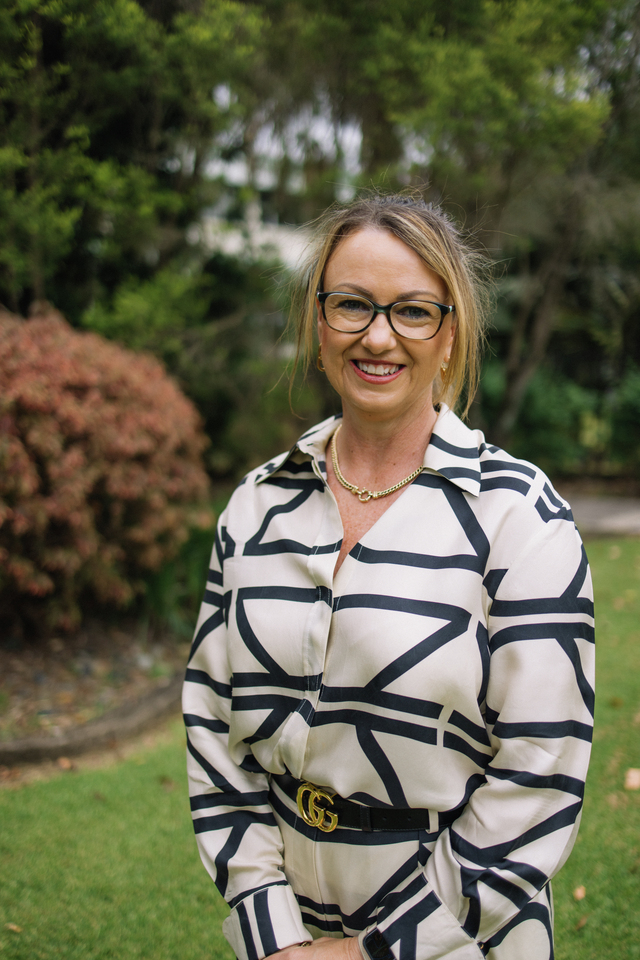 Narelle Pearse standing in front of greenery smiling at the camera with hands placed in front of her