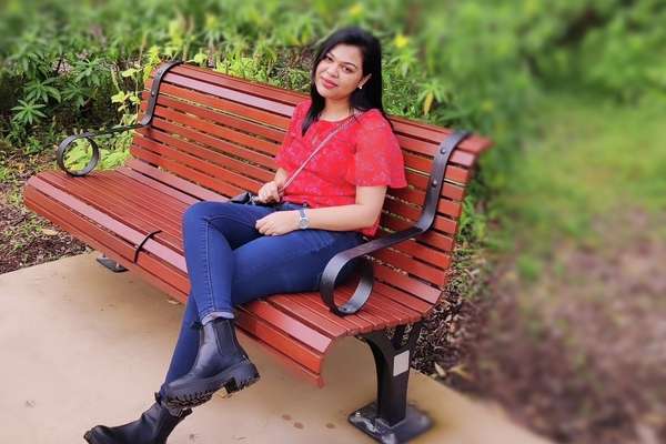 International student Nawrin Tabbasum sitting on a park bench with green shrubs in the background