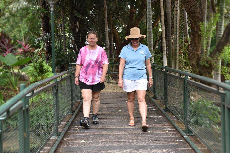 Two women walk across footbridge amongst lush tropical gardens