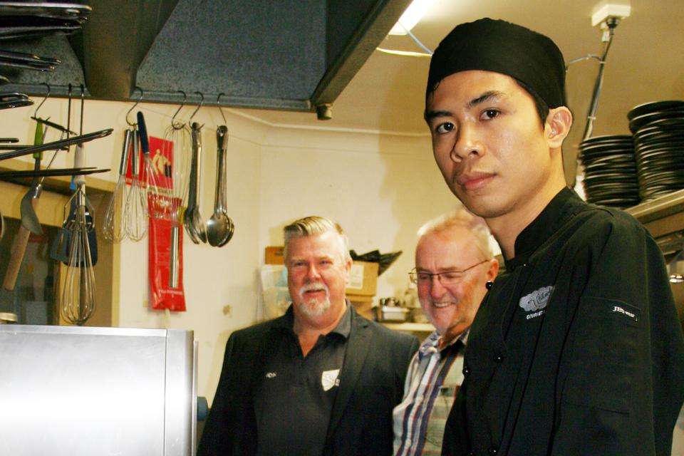 Image of an Asian man standing in a kitchen with two other men