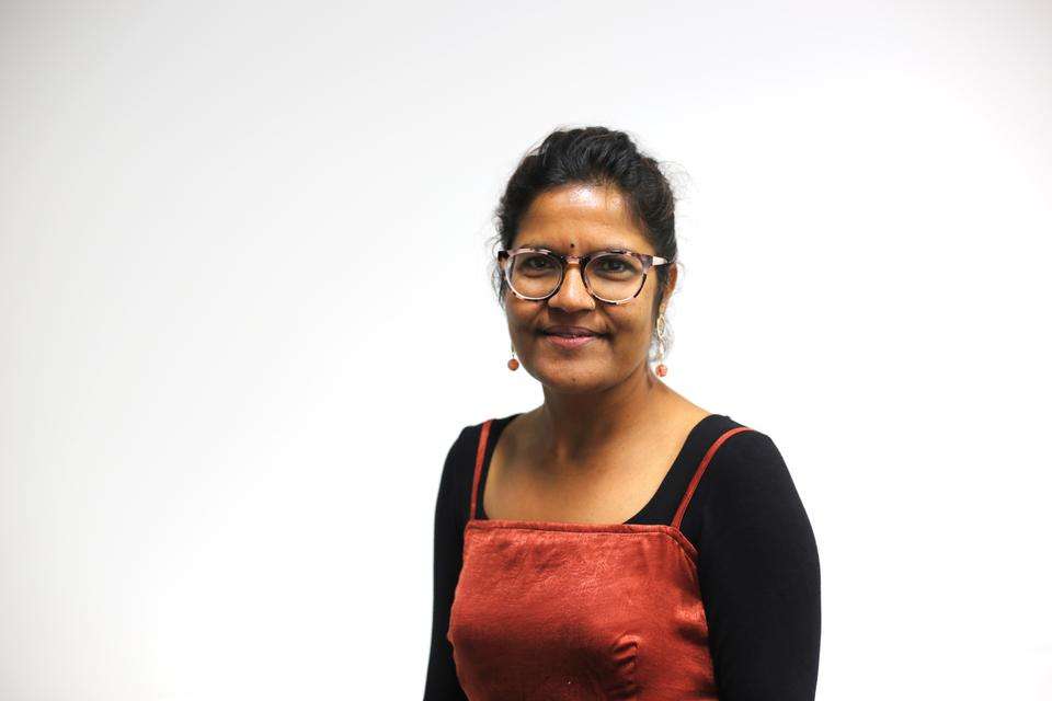 Sabi Kaphle stands in front of white wall, smiling.