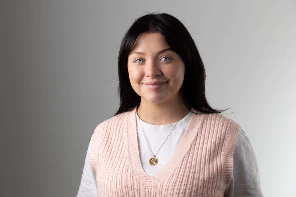 Dayna Easton smiling, in front of grey wall.