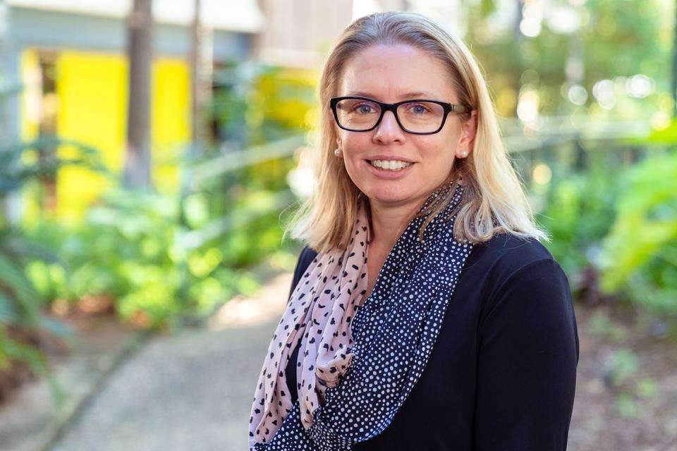 Dr Amy Johnson stands in an outdoor setting, she wears a dotted scarf and dark-rimmed glasses.