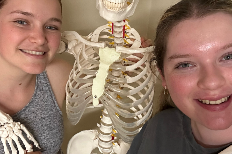 Two young women posing with a skeleton