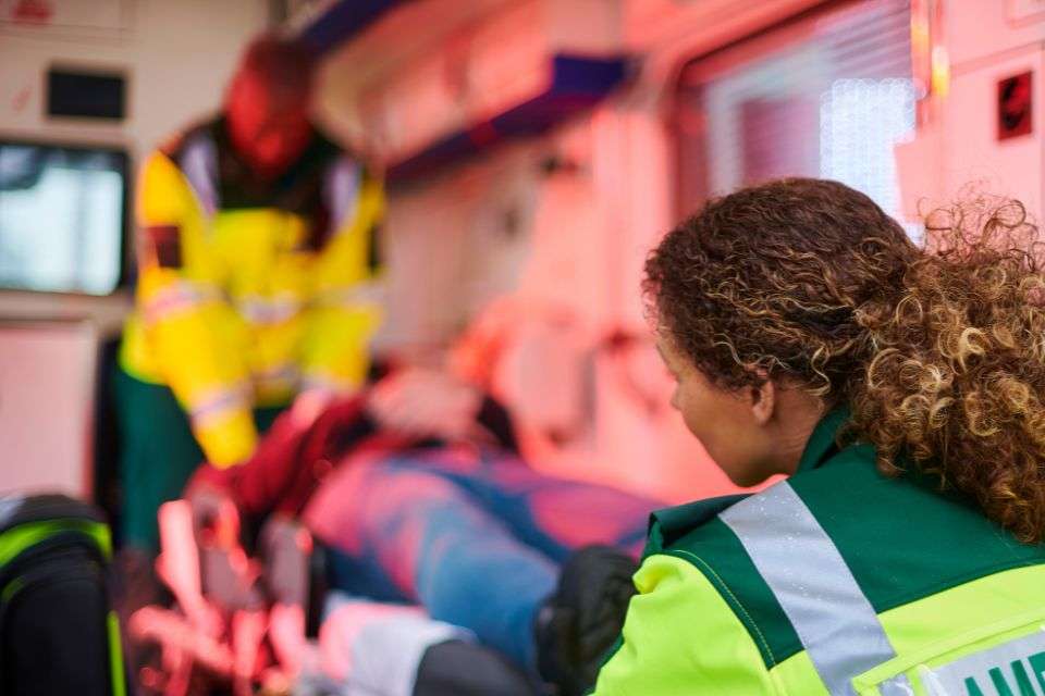 A woman in high vis assiting a man in a stretcher with her male colleague