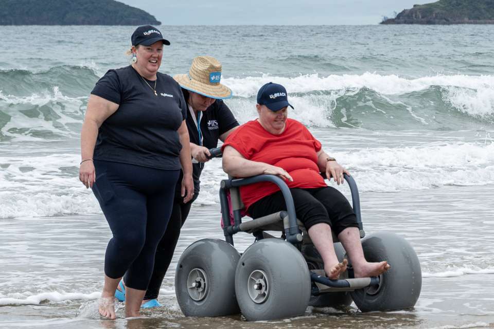 Sasha Job and volunteer pushing a woman in a beach wheelchair