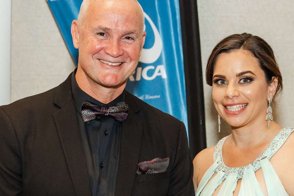 Man in black suit standing next to woman in a gown holding an award