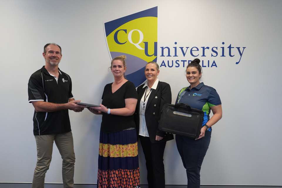 Man passing a laptop to a woman next to two additional women