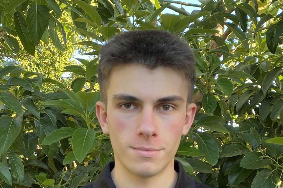 Man in black polo shirt in front of foliage