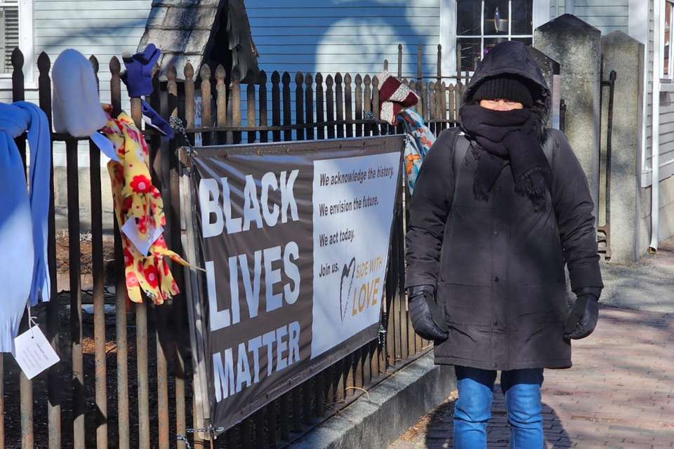 Woman in a large black coat next to a fence with signage