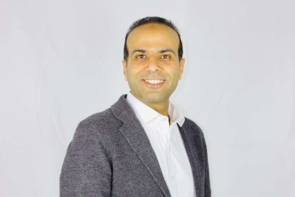 Man in grey suit jacket and whit button up smiling at camera
