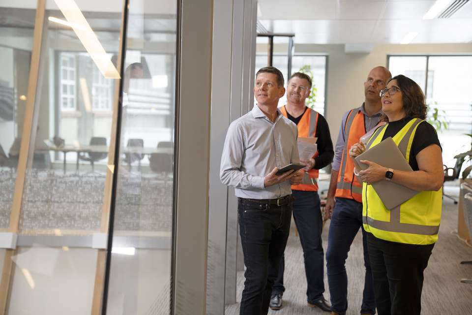 A group of workers discussing building plans looking outside of window of building.