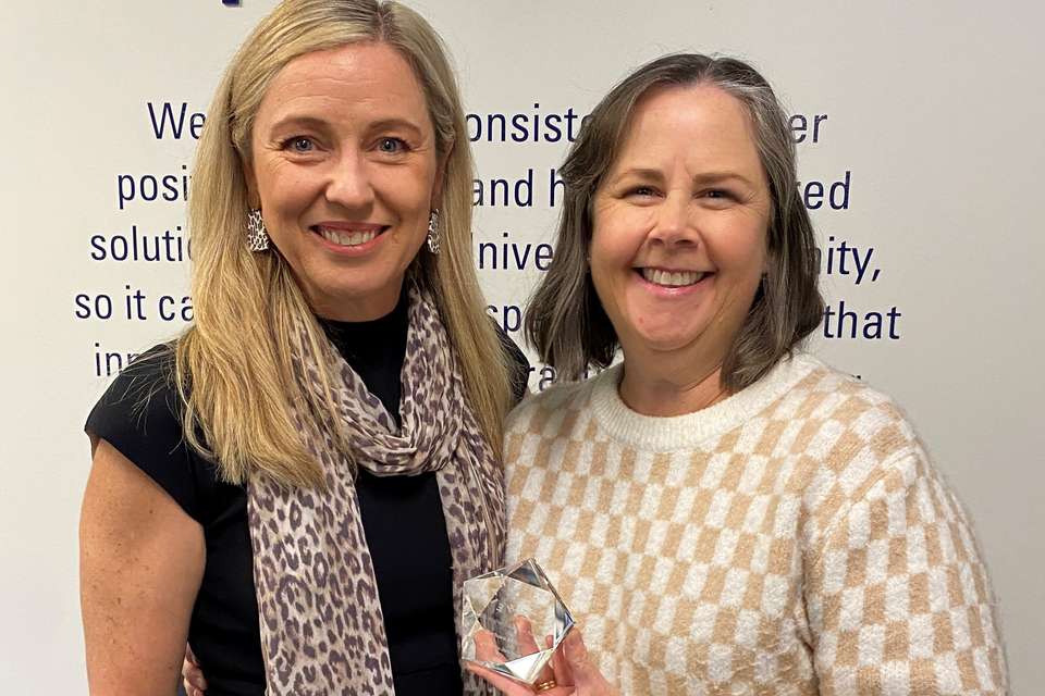 Two women smiling at camera with one holding an award