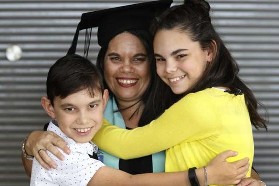 Woman in regalia hugging two children