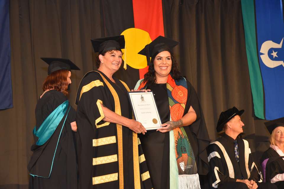 Two women in regalia holding a certificate together