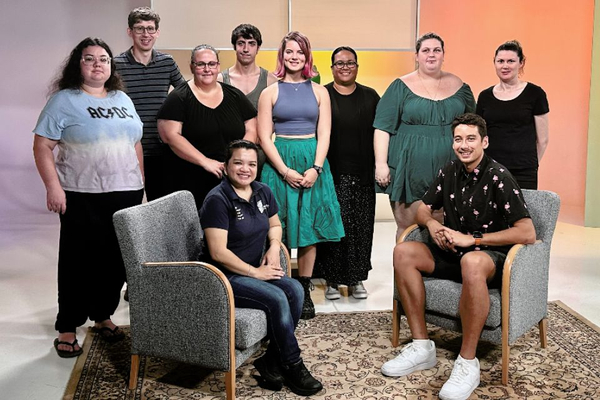 A group of eight students stand in a TV student, with a CQU lecturer and alumnus seated in front of them.