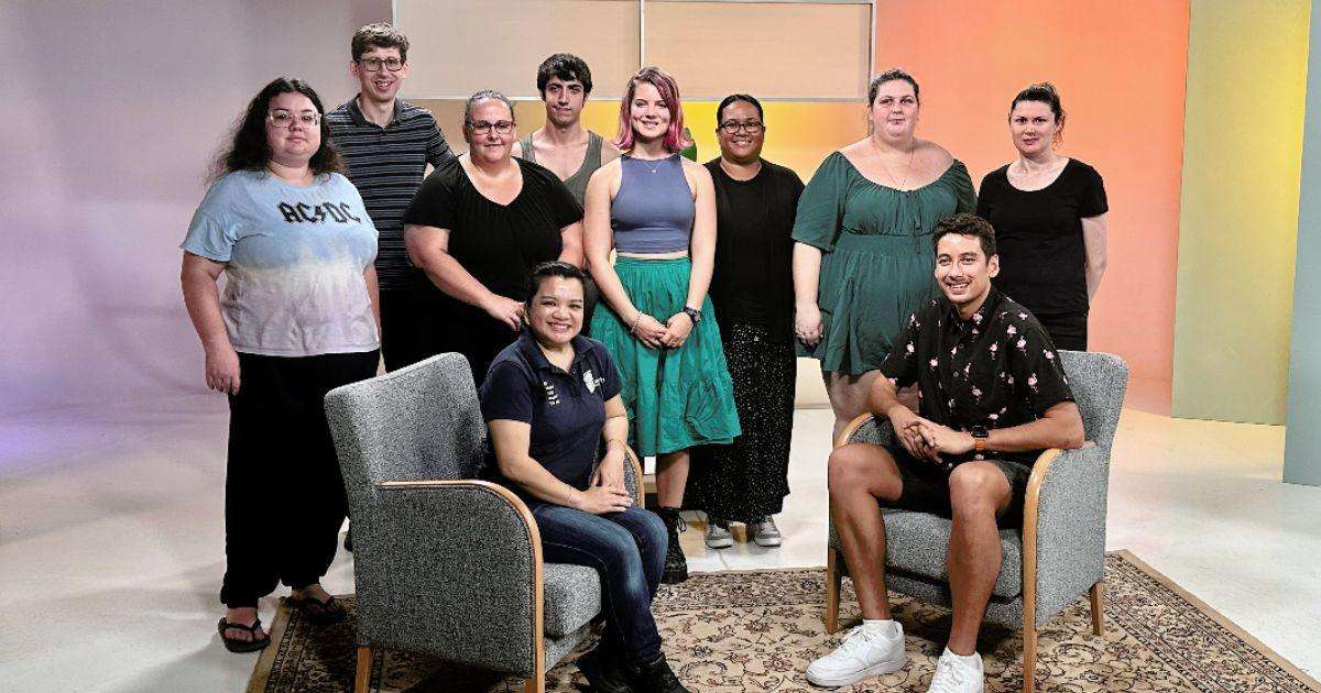 A group of eight students stand in a TV student, with a CQU lecturer and alumnus seated in front of them.