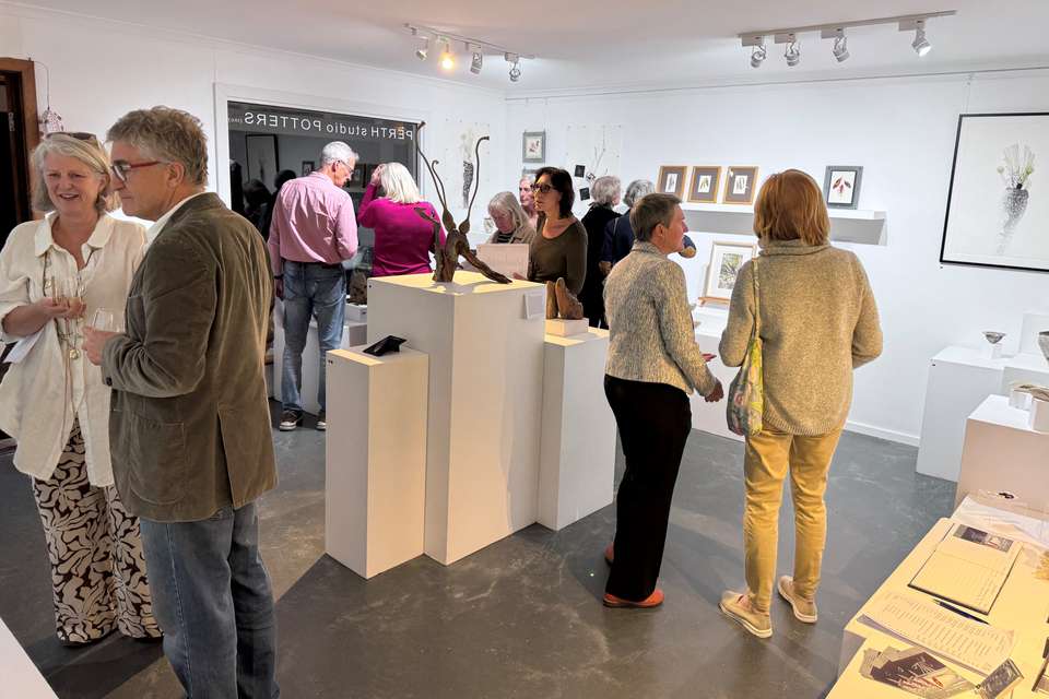 An art gallery exhibition room in full swing with guests mingling and viewing a colletion of mixed media artworks.