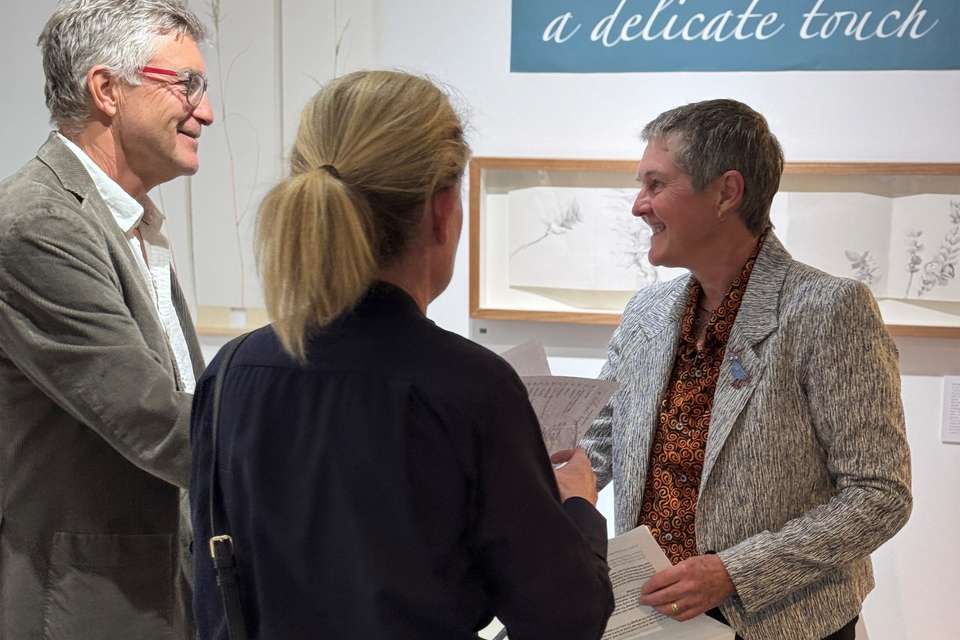 Artist Jenny Gilberston stands in an art gallery amidst works in her exhibition, greeting guests at her opening show.