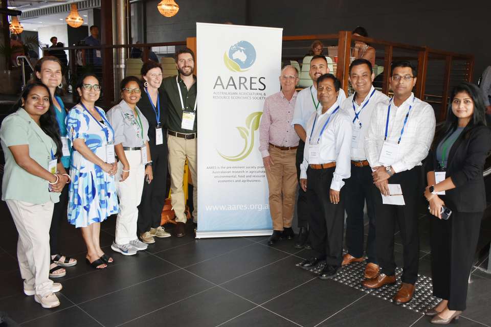 Image of a group of CQUniversity academics and researchers standing beside a banner on the AARES Conference