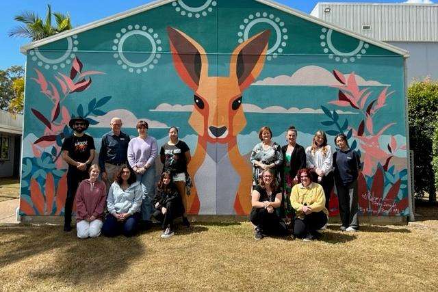 A group of students stand in front of a brightly coloured mural featuring a kangaroo. They are joined by a representative from Bundaberg Regional Council and CQUniversity.