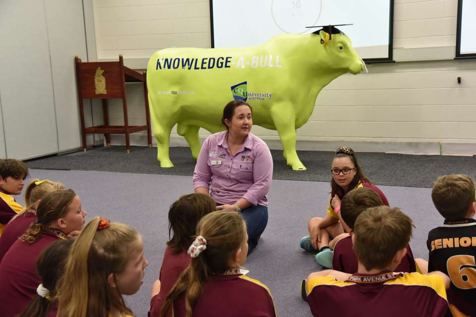 Dr Jaime Manniung sits on the floor teaching school students with a fake bull in the background.JPG