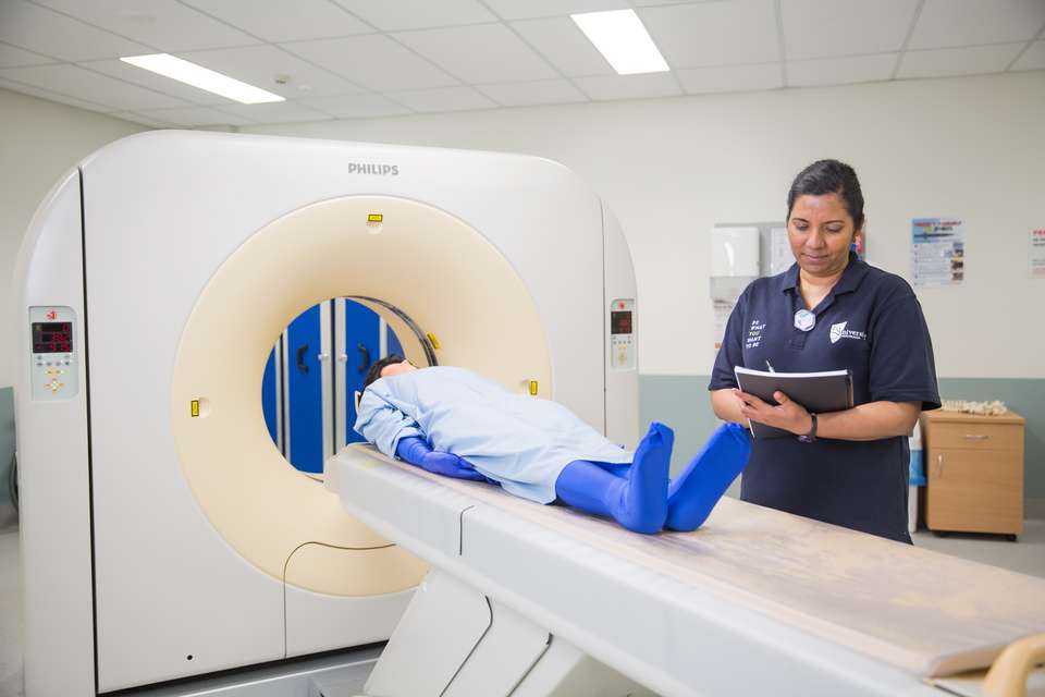 A student in a CQUniversity blue shirt with a dummy on a scanner bed in a radiology lab.jpg