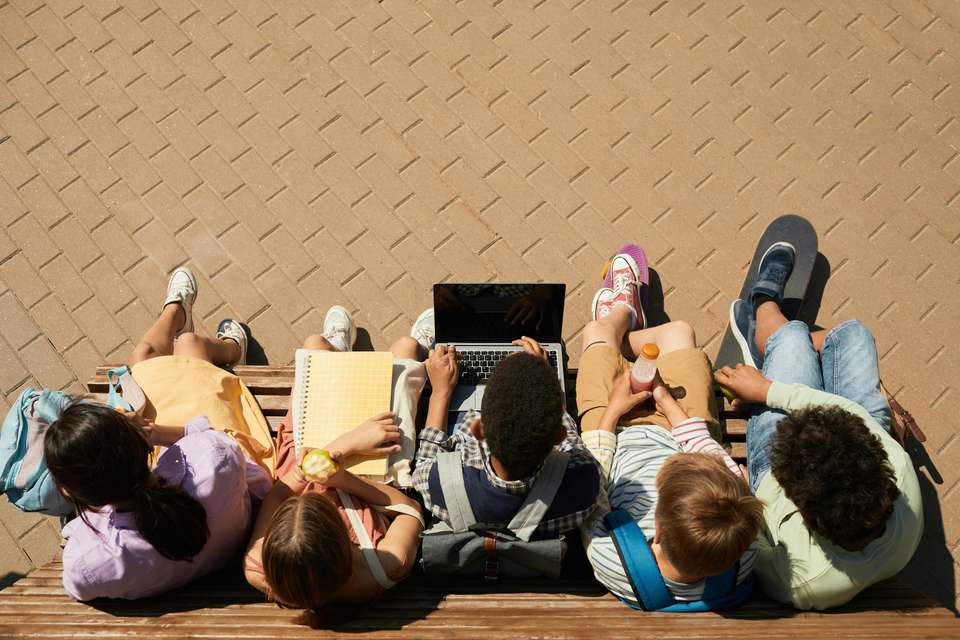 Aerial shot of school students sitting on a bench with their backpacks, laptops, notebooks and snacks