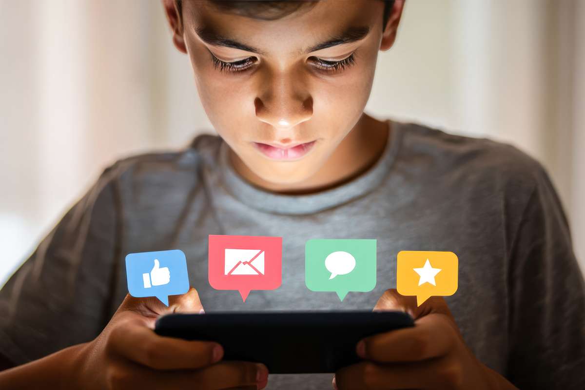 Young teen boy with grey tshirt holds a phone with social media symbols popping out