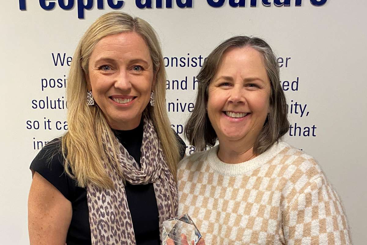 Two women smiling at camera with one holding an award
