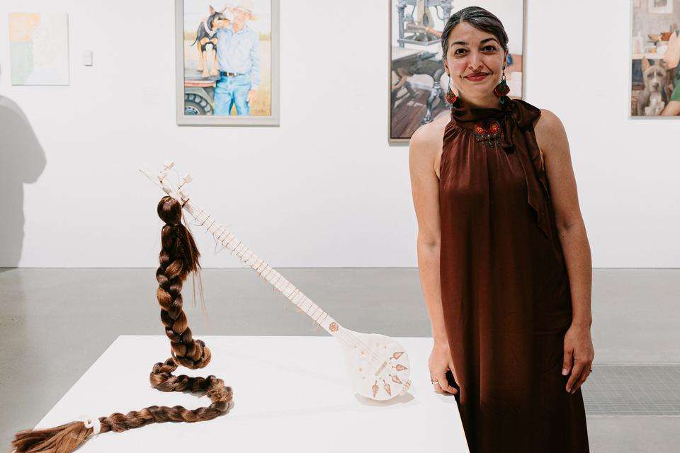 Winner Niloufar Lovegrove stands smiling in a long red dress next to her sculpture