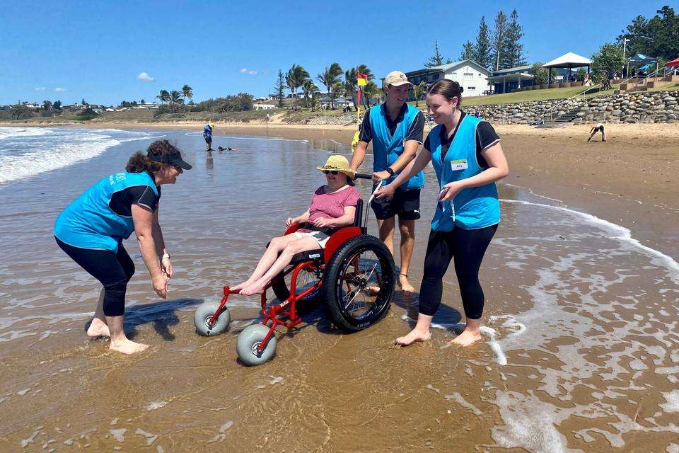 CQU Physiotherapy students assisting a woman in a beach wheelchair on the shore.jpg