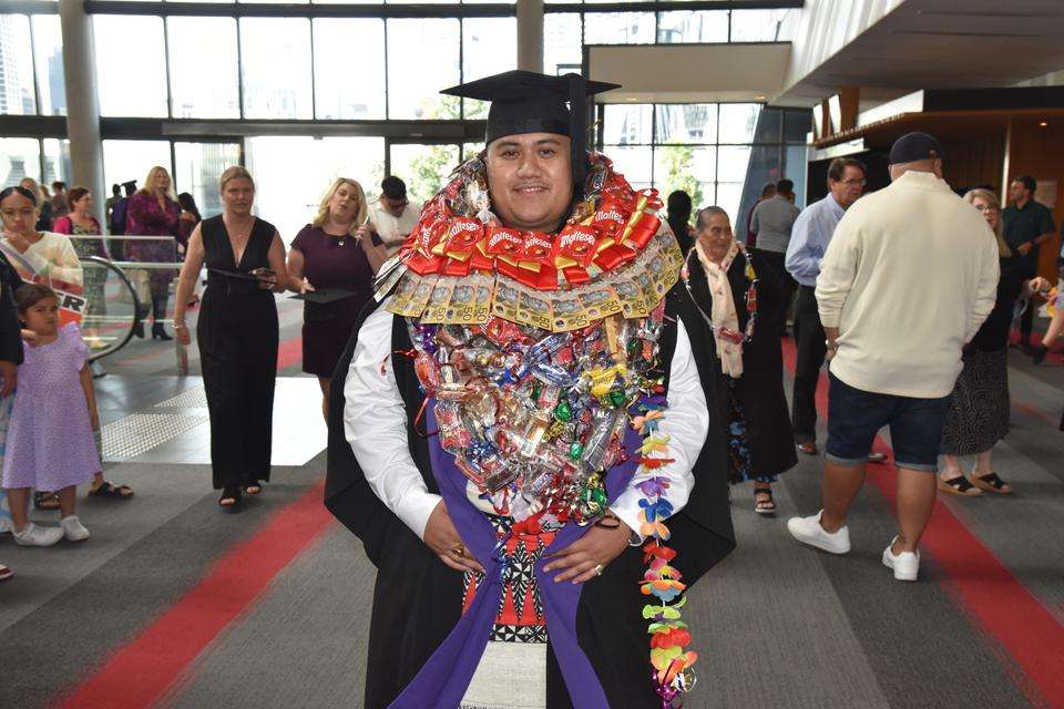 Image of a Samoan man in graduation attire and also wearing a lei looking at the camera