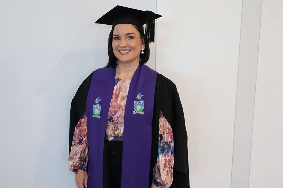 A woman in ceremonial graduation attire is smiling at the camera