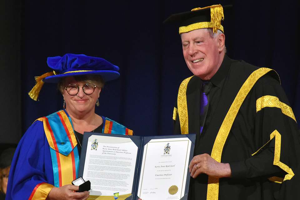 A woman and a man in ceremonial graduation garb holding a certificate