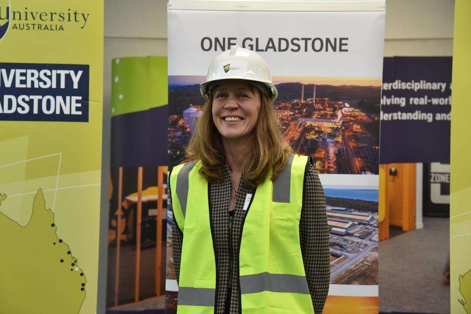 Dr Cal Devney wears a hard hat and hi vis vest and stands in front of a corporate banner at a media event for the hydrogen central information centre