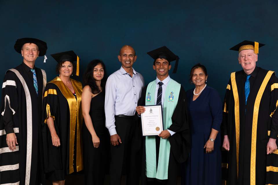 A young man (Chamika) is pictured in graduation robes holding a testamur alongside his  parents and sister and the University's Vice-Chancellor, Deputy Chancellor and Chancellor.