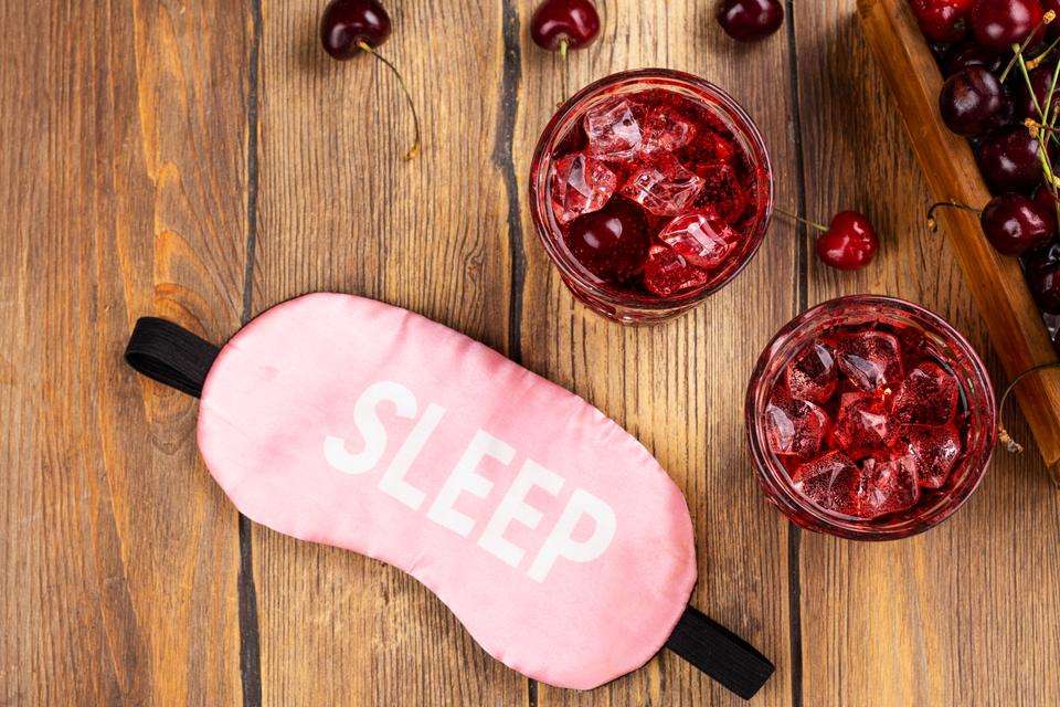 A sleep mask and two red mocktails surrounded by cherries
