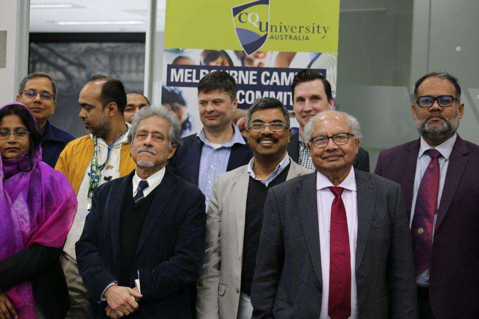 A group of ten people stand in a group in front of a banner that says CQUniversity Australia.