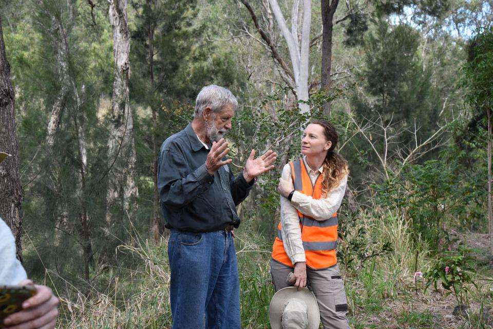 Two people stand talking amongst native bushland