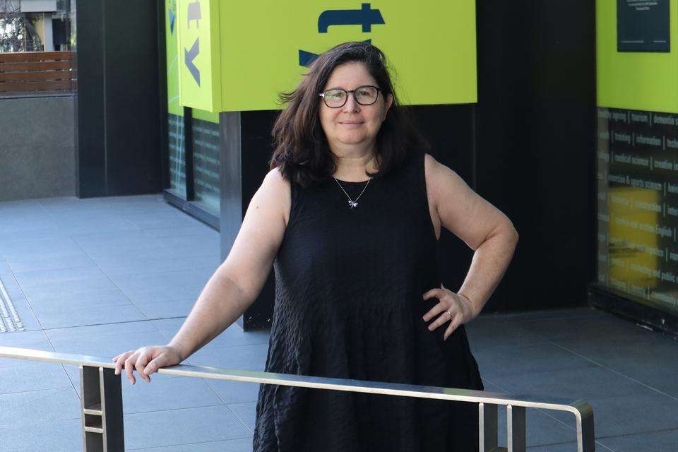 Image of a woman in a black dress and wearing glasses standing outside her hand on a railing