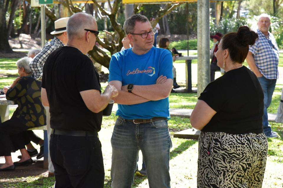 Man with blue tshirt withe EndLoneliness on front talks with two people in a garden setting.jpg