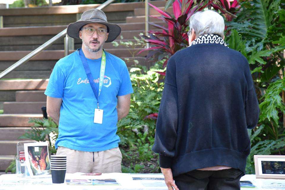 Man with blue tshirt with end loneliness on it with hat talks with older person over a table displaying information.jpg