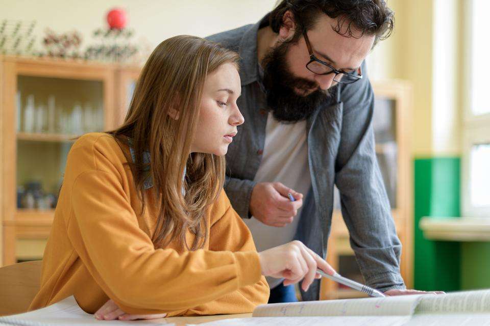 Young male teacher helping his female student in chemistry class