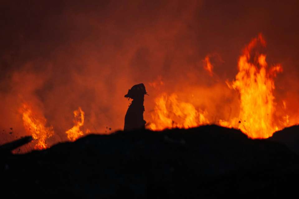 A silouhette of a lone firefighter against a backdrop of roaring flames.