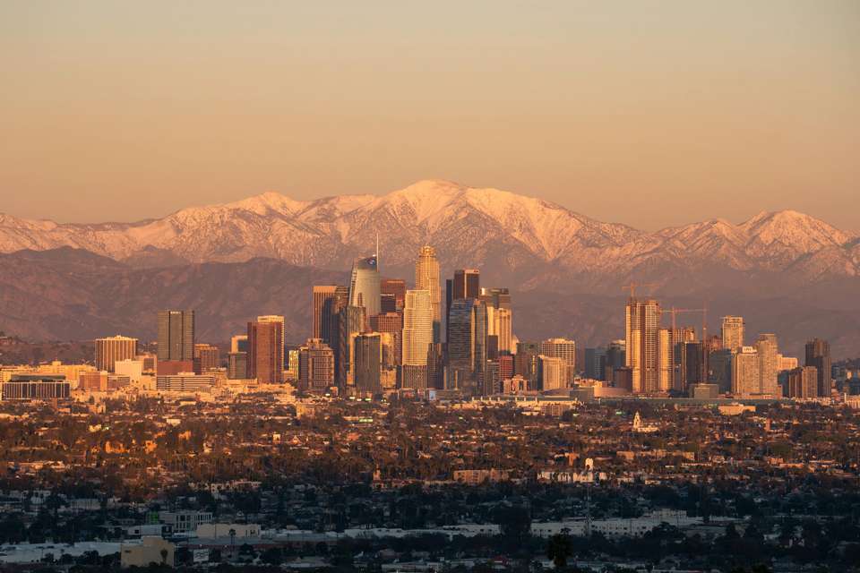 A wide scoping shot of Los Angeles, framed by its towering snowy mountains in the background