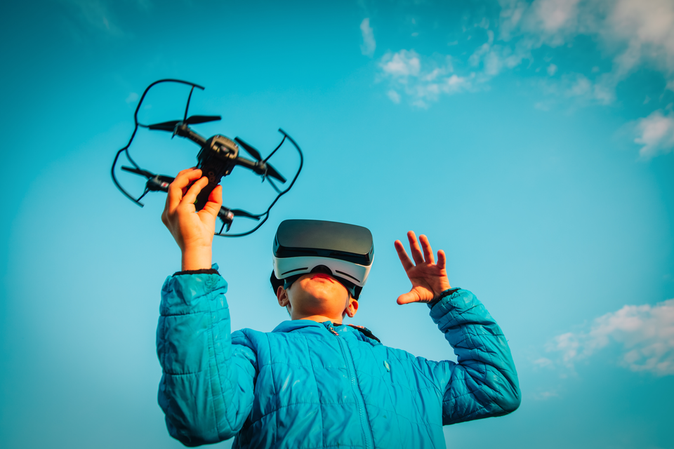 Image of a boy wearing a blue jacket, VR headset and holding a drone